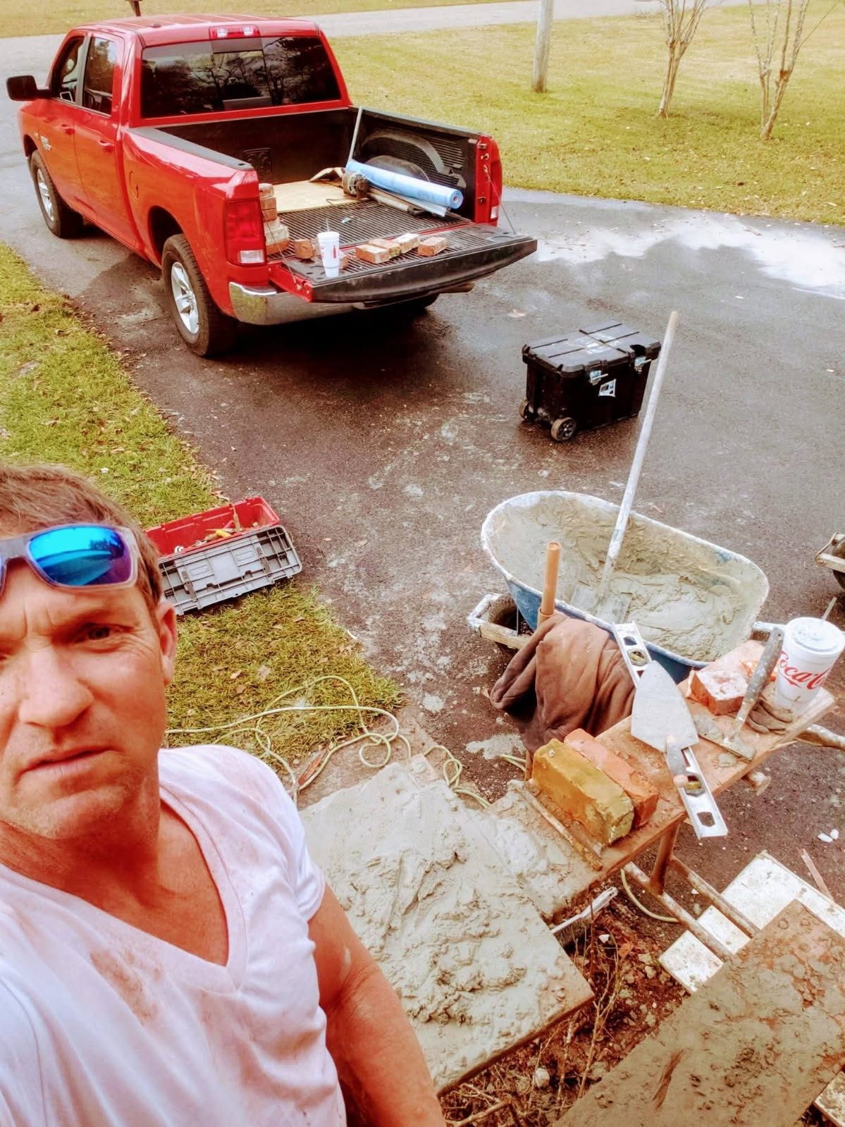 A selfie on the job, with brick in the bed of a red pickup and mortar in the wheelbarrow