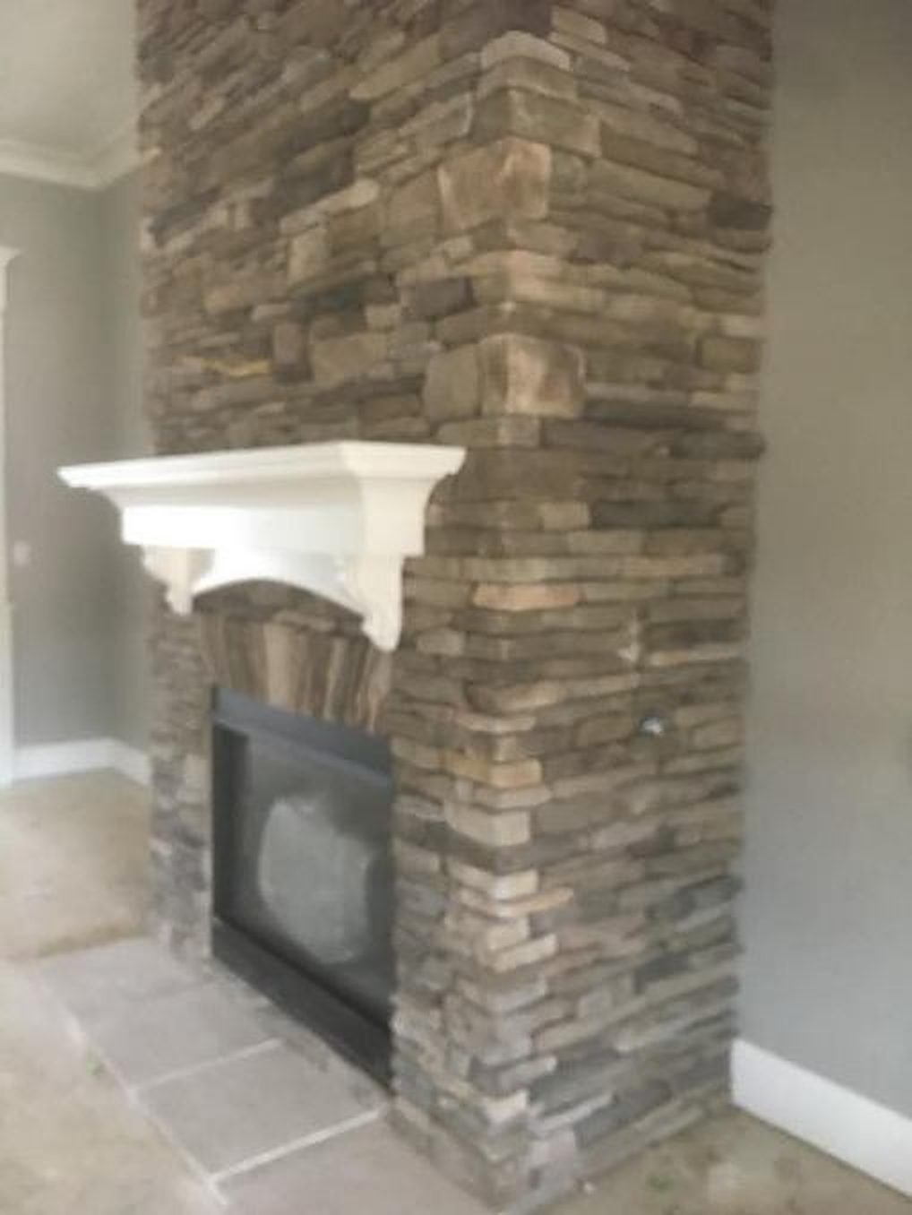 A stacked stone fireplace with a white wood mantel