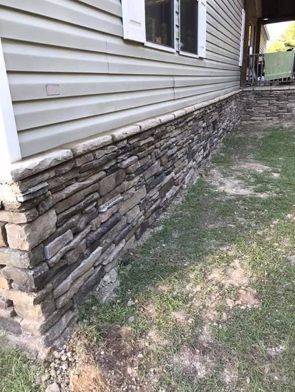 Stacked stone along the bottom of a house with vinyl siding