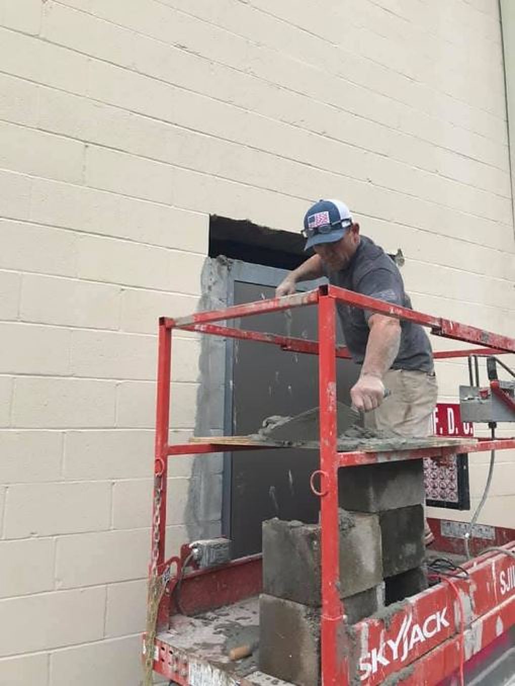 A mason on a lift laying block to close up a door opening in a block wall