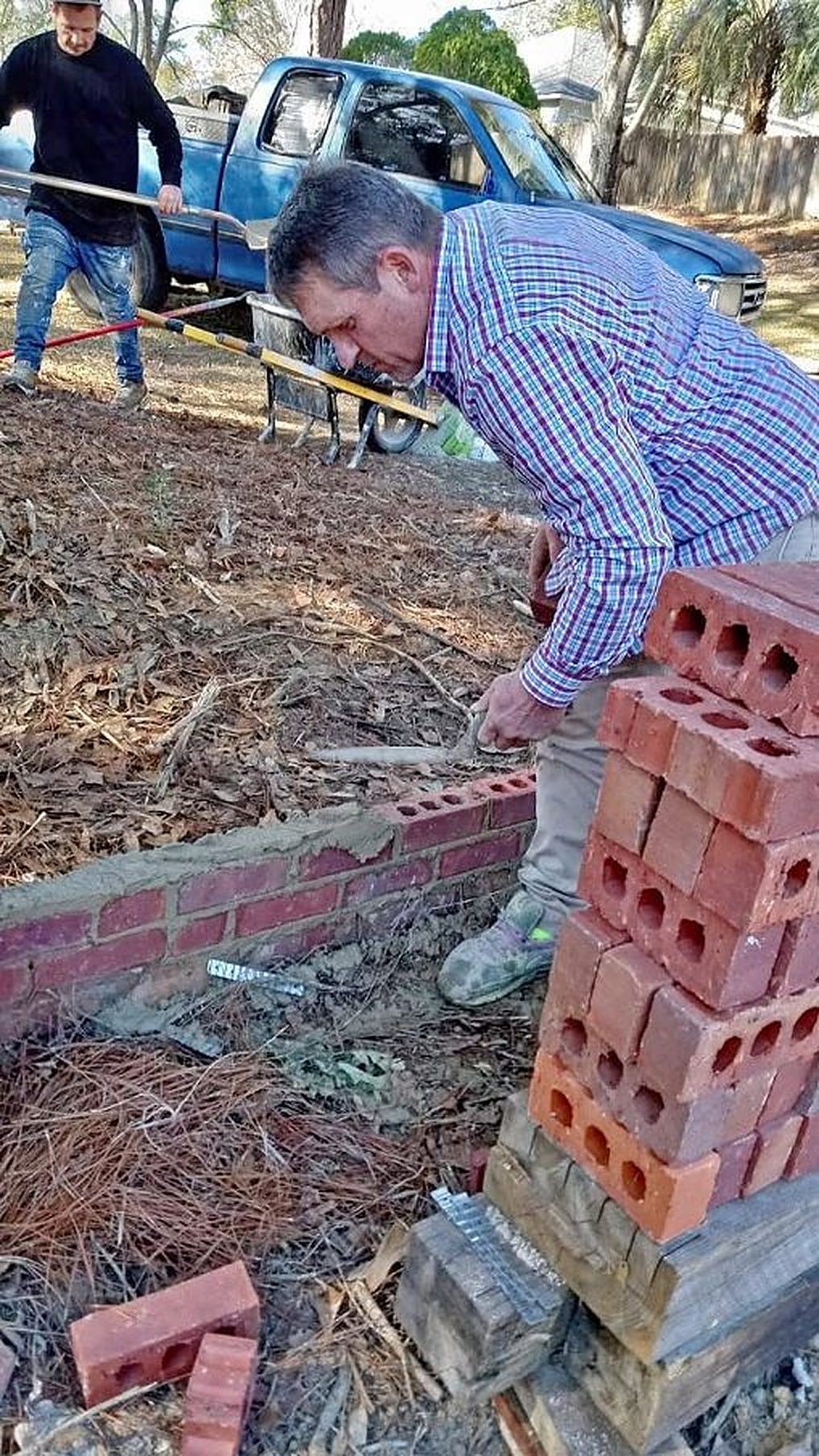 A mason laying a low brick wall along a planting bed