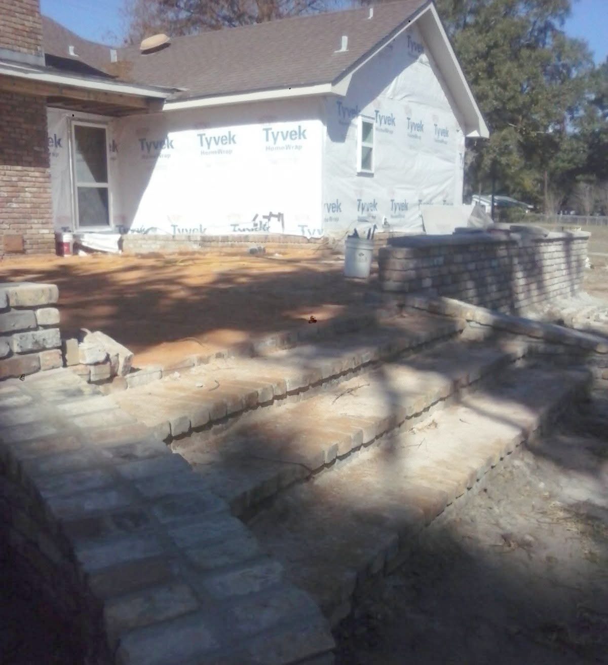 New brick steps and low brick walls beside an addition still in house wrap