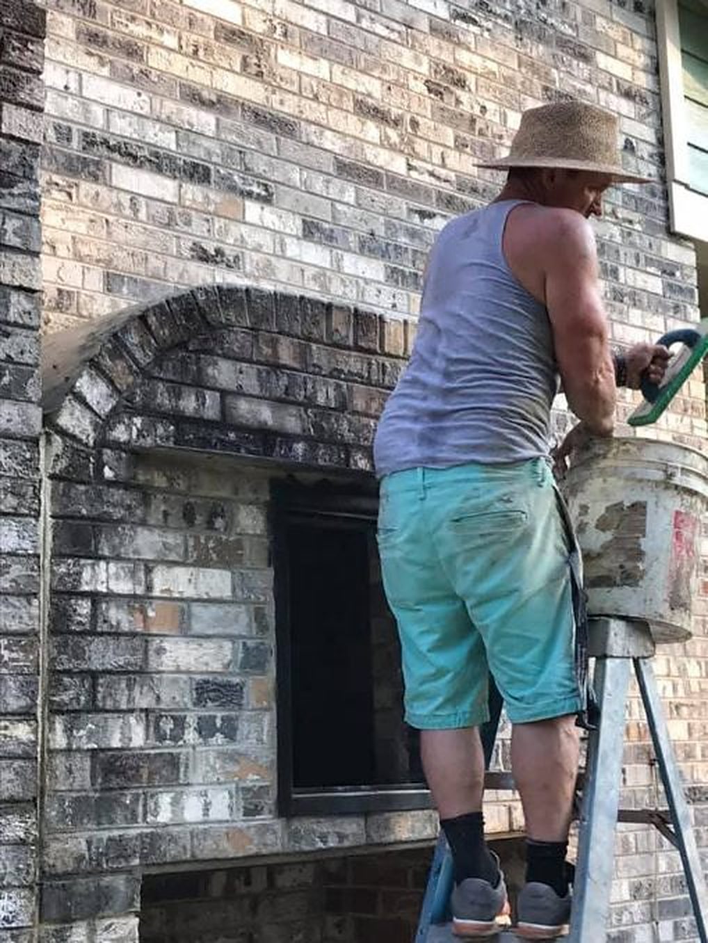 A mason on a ladder working on the joints around an arched opening in old painted brick