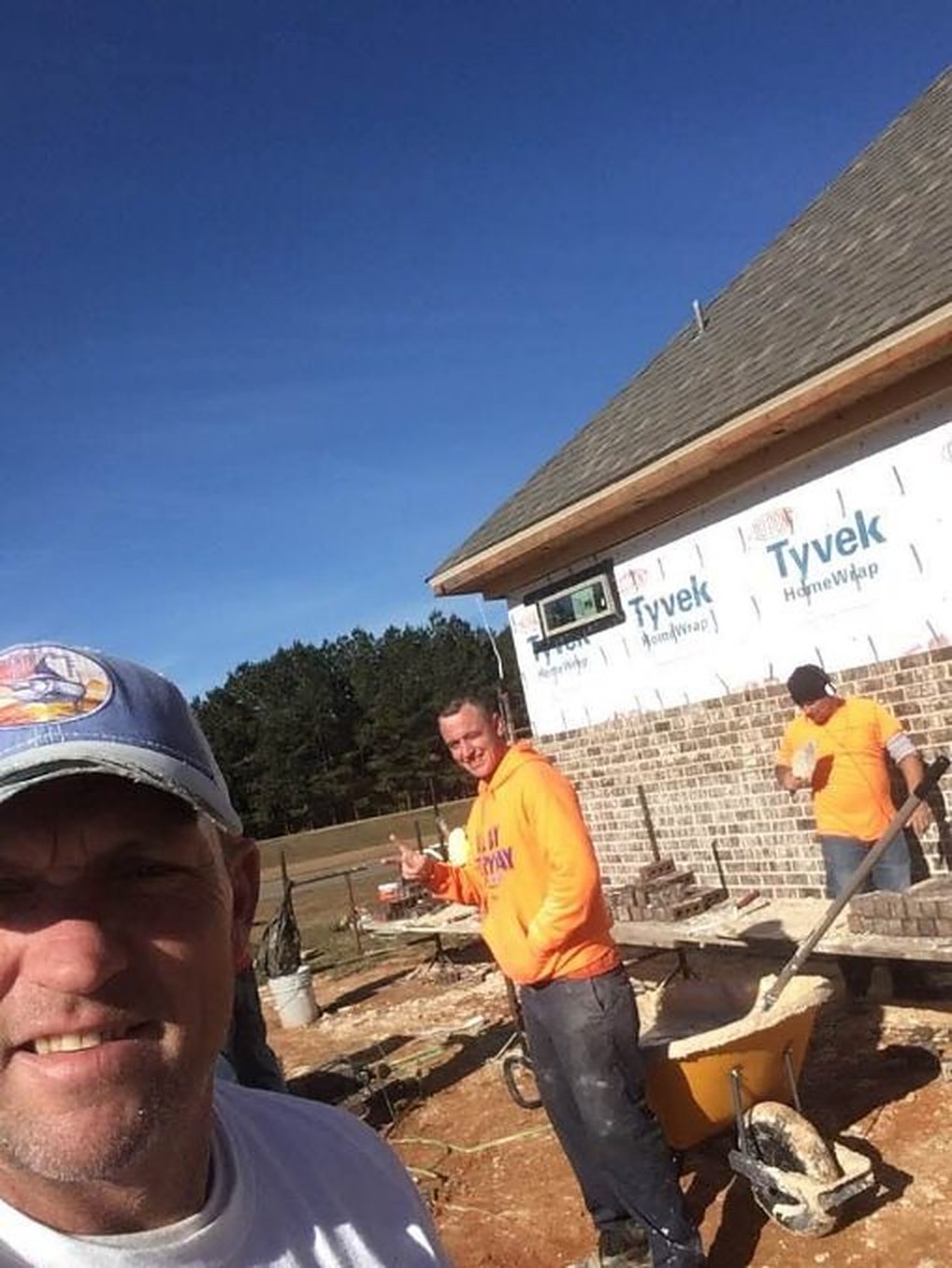 A selfie on the job, with the crew laying brick on a new addition behind