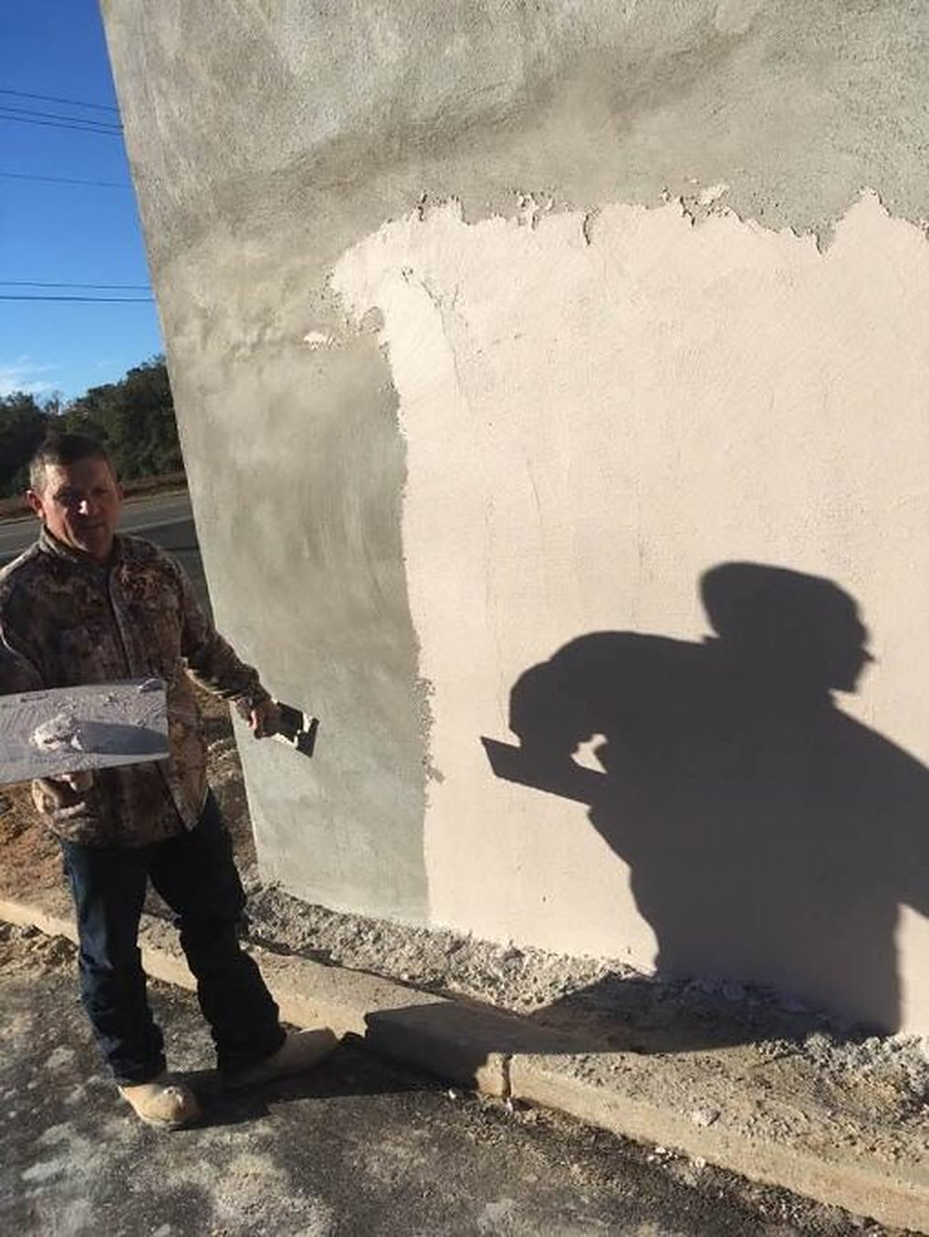 A mason with a hawk and trowel spreading a coat of cement over a block wall