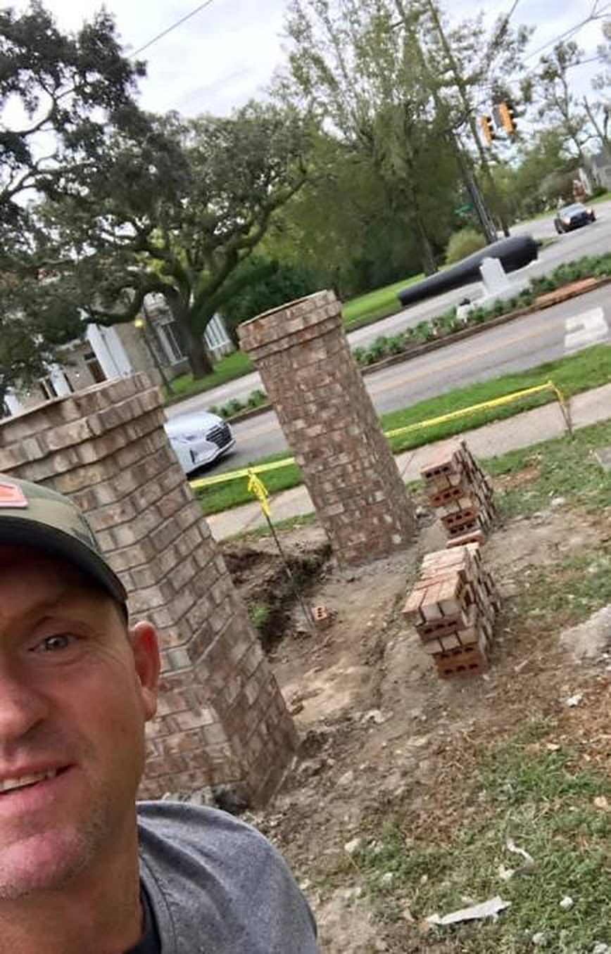 A selfie beside two brick columns going up for a business sign by the road